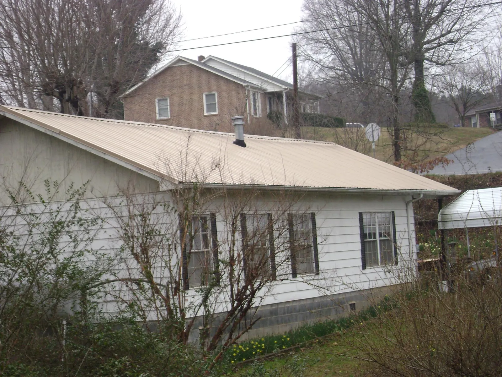 Tan metal roof on a white sided house set into a hillside — Commercial Roofing by Roofing Brothers in Toquerville